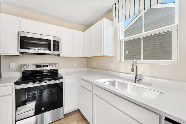 kitchen featuring appliances with stainless steel finishes, white cabinets, light countertops, and a sink