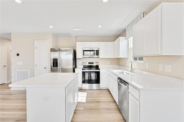 kitchen with stainless steel appliances, light wood finished floors, a kitchen island, and a sink