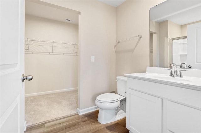 full bath featuring a spacious closet, toilet, vanity, wood finished floors, and baseboards