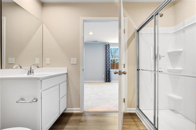 full bathroom with wood finished floors, a shower stall, vanity, and baseboards