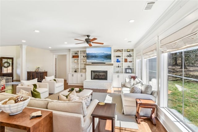 living area with a fireplace with raised hearth, decorative columns, visible vents, and a healthy amount of sunlight