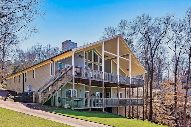 rear view of house with a yard, a chimney, a ceiling fan, a deck, and stairs