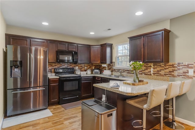 kitchen featuring light wood-style flooring, dark brown cabinetry, a peninsula, a sink, and black appliances