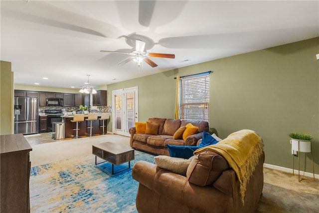 living room featuring baseboards, light colored carpet, and ceiling fan with notable chandelier