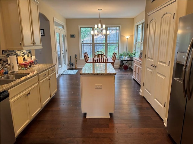 kitchen featuring dark wood finished floors, decorative backsplash, a kitchen island, stainless steel appliances, and a sink