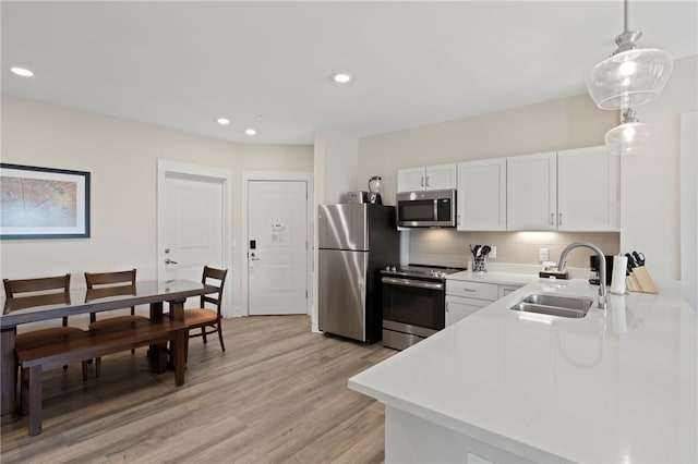 kitchen featuring light wood finished floors, light countertops, backsplash, appliances with stainless steel finishes, and a sink