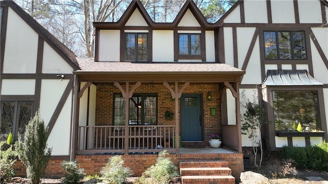 view of front facade with covered porch, brick siding, a shingled roof, and stucco siding