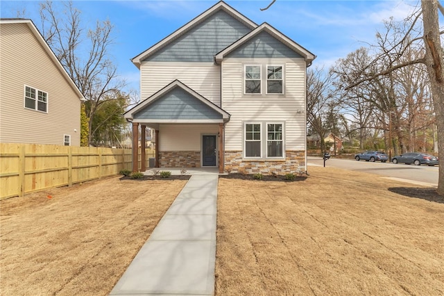 view of front facade featuring stone siding, a porch, and fence