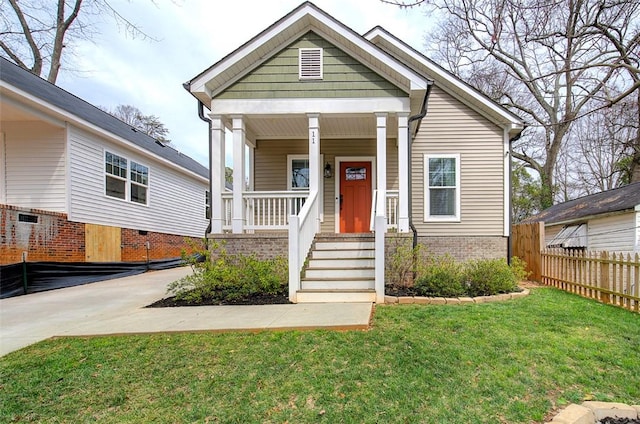 view of front of house featuring a porch, brick siding, fence, and a front lawn