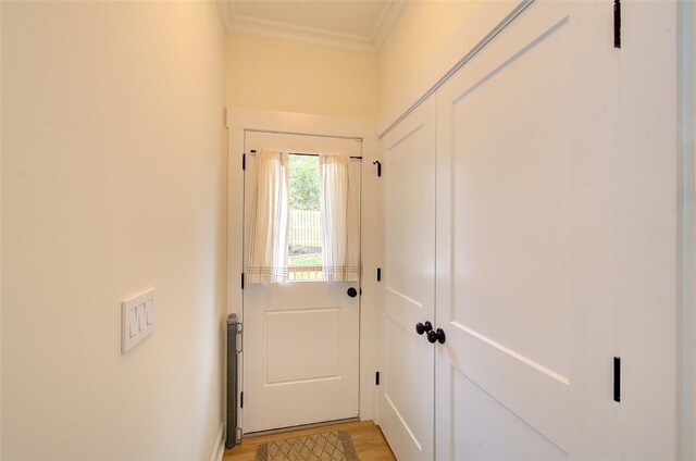 doorway with light wood finished floors and ornamental molding