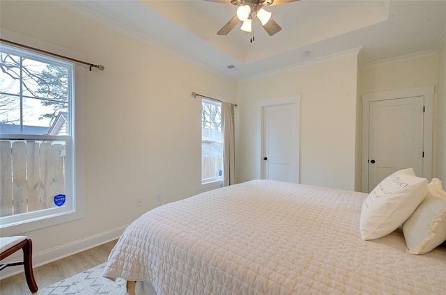 bedroom with a tray ceiling, ornamental molding, ceiling fan, light wood-type flooring, and baseboards