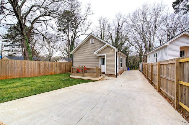 rear view of property featuring a yard, concrete driveway, a fenced backyard, and a wooden deck