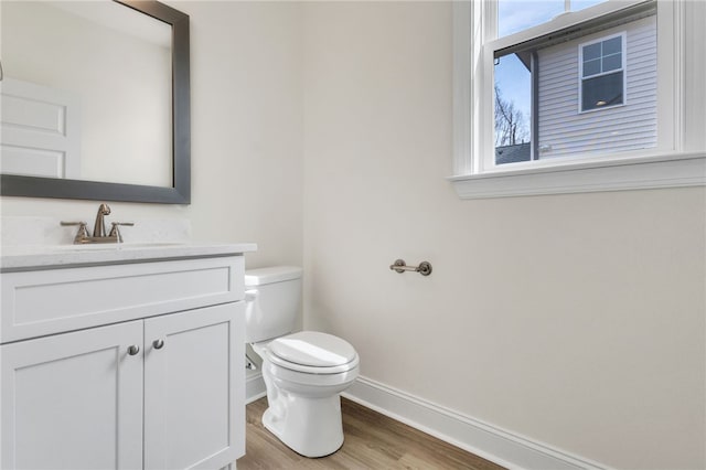 half bathroom with wood finished floors, vanity, toilet, and baseboards