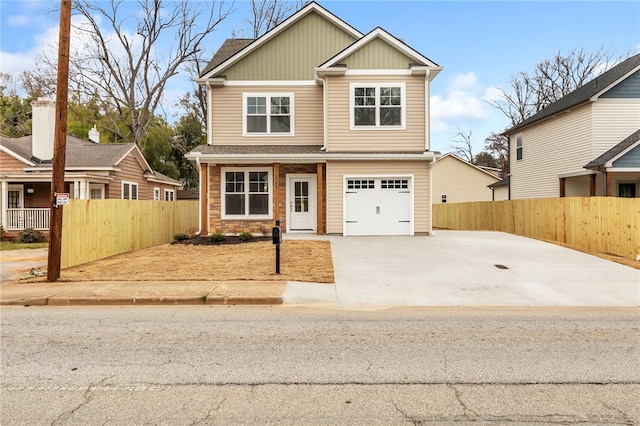 craftsman-style home with driveway, stone siding, fence, and board and batten siding