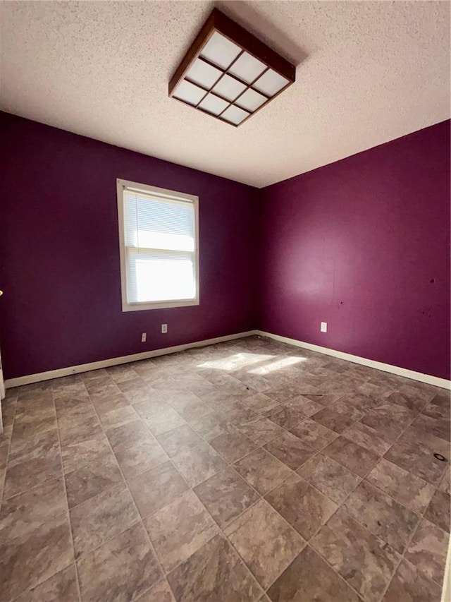 unfurnished room with a textured ceiling and baseboards