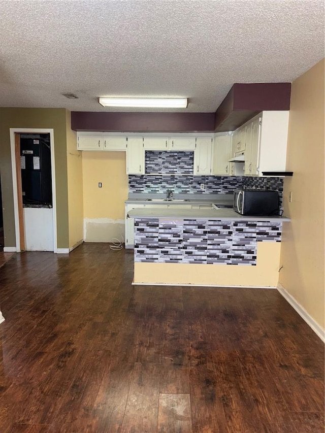 kitchen featuring under cabinet range hood, stainless steel microwave, decorative backsplash, and dark wood-style flooring