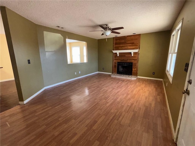 unfurnished living room featuring a textured ceiling, a fireplace, wood finished floors, a ceiling fan, and baseboards