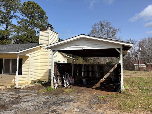 view of home's exterior featuring a carport, fence, a shingled roof, and dirt driveway