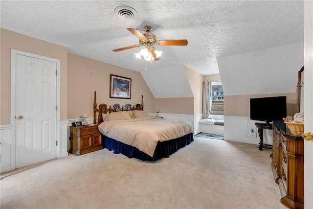 bedroom featuring a wainscoted wall, lofted ceiling, light colored carpet, visible vents, and ceiling fan