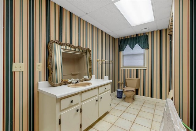 bathroom with wallpapered walls, visible vents, a drop ceiling, toilet, and vanity