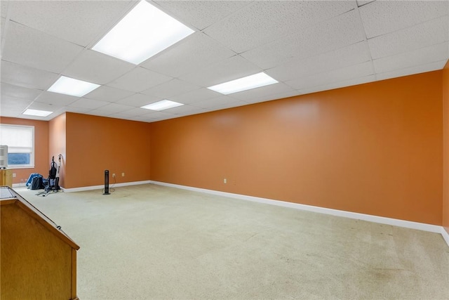 interior space featuring baseboards, a drop ceiling, and light colored carpet