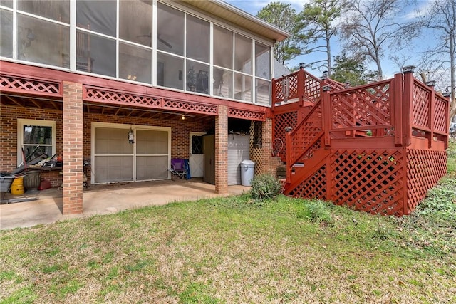 rear view of property with driveway, a garage, a sunroom, stairs, and brick siding