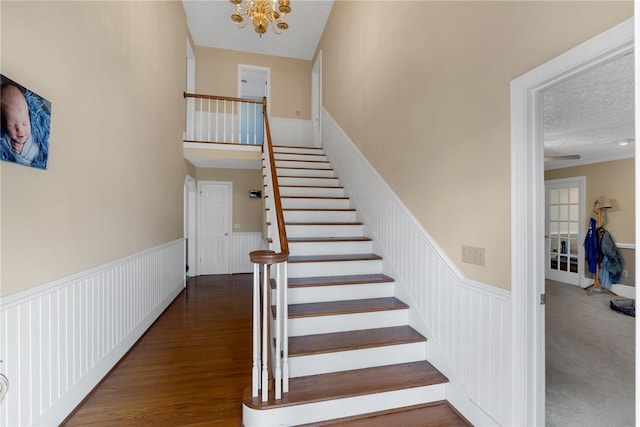 stairs with a textured ceiling, wainscoting, wood finished floors, and an inviting chandelier