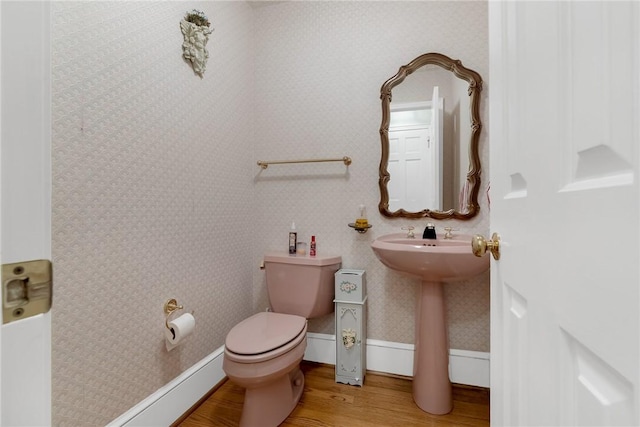 half bathroom with baseboards, wood finished floors, toilet, and wallpapered walls