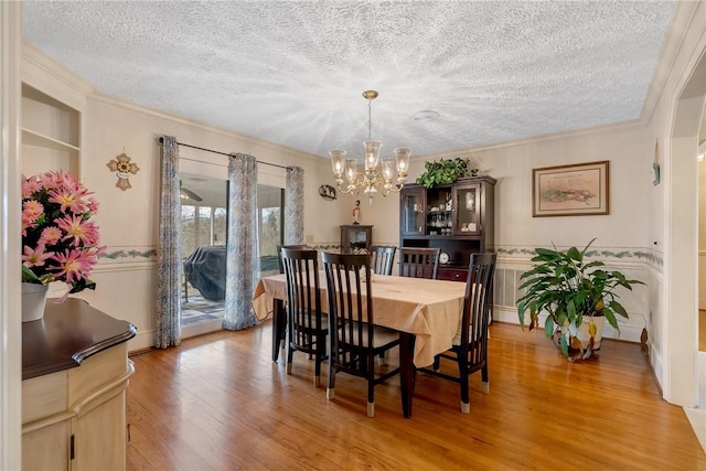 dining room featuring a wainscoted wall, crown molding, light wood finished floors, an inviting chandelier, and a textured ceiling