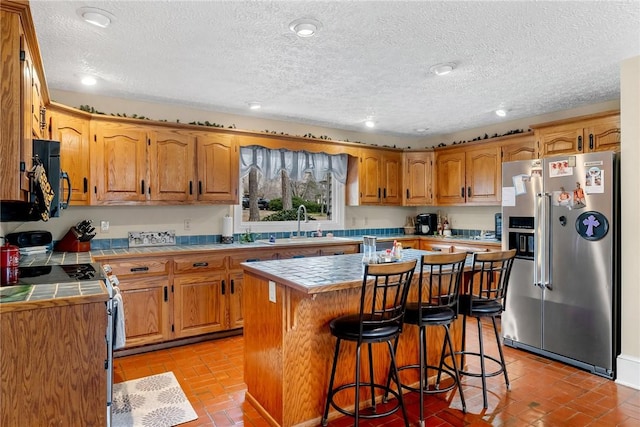 kitchen with black microwave, range with electric stovetop, tile countertops, and stainless steel fridge with ice dispenser