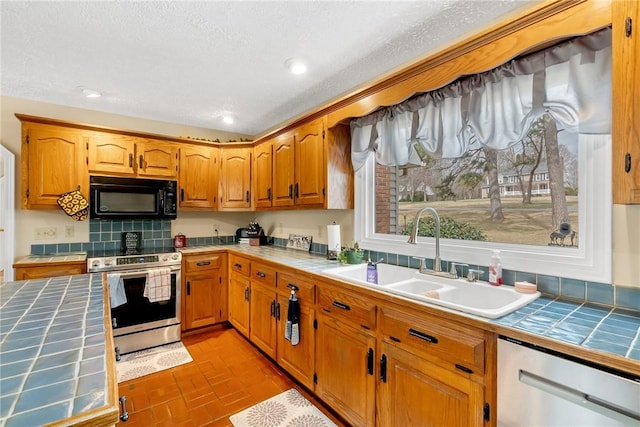 kitchen featuring tile countertops, stainless steel appliances, brick floor, and a sink