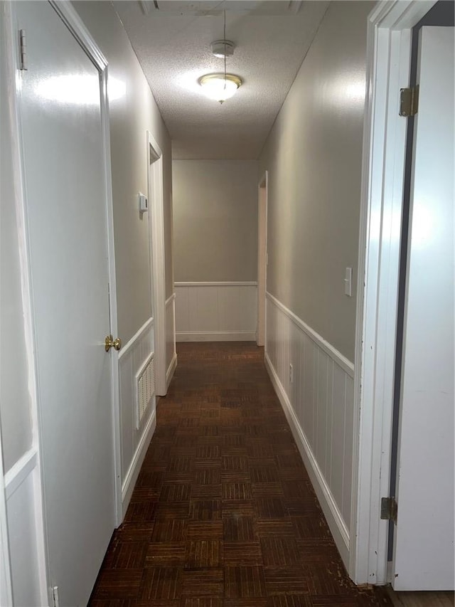 hallway featuring a textured ceiling, wainscoting, and visible vents