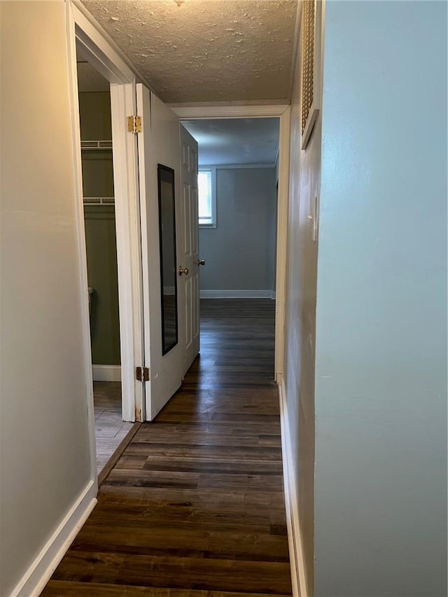 corridor featuring a textured ceiling, dark wood finished floors, and baseboards