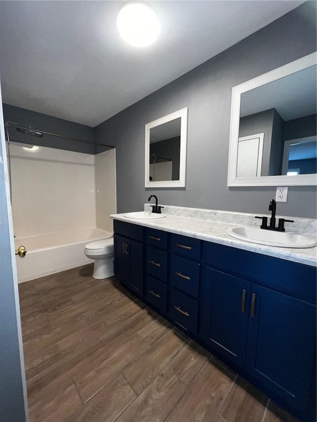 full bath with toilet, double vanity, a sink, and wood finished floors