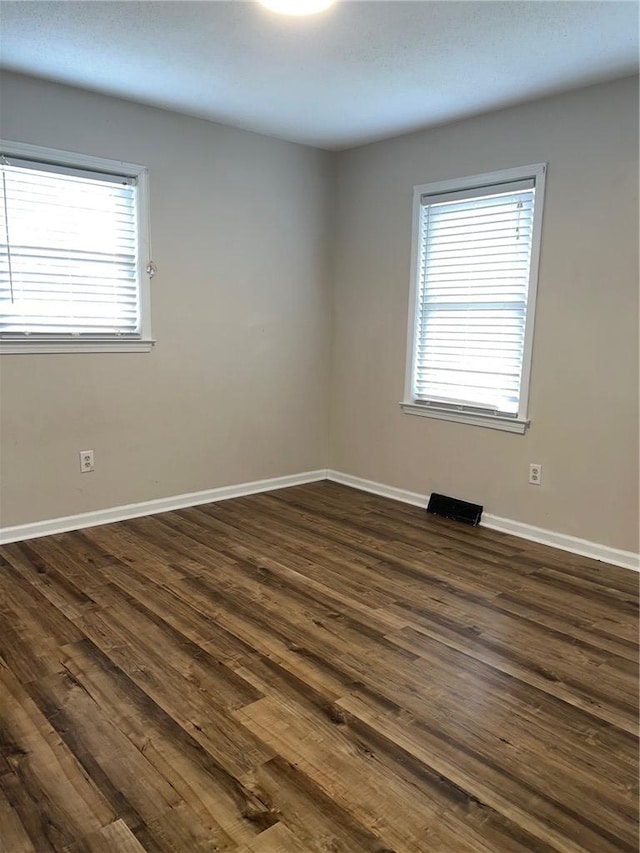 empty room with visible vents, dark wood finished floors, and baseboards