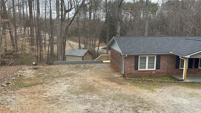 view of home's exterior with a shingled roof, dirt driveway, and brick siding