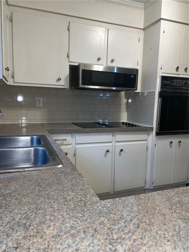 kitchen with tasteful backsplash, white cabinets, a sink, and black appliances