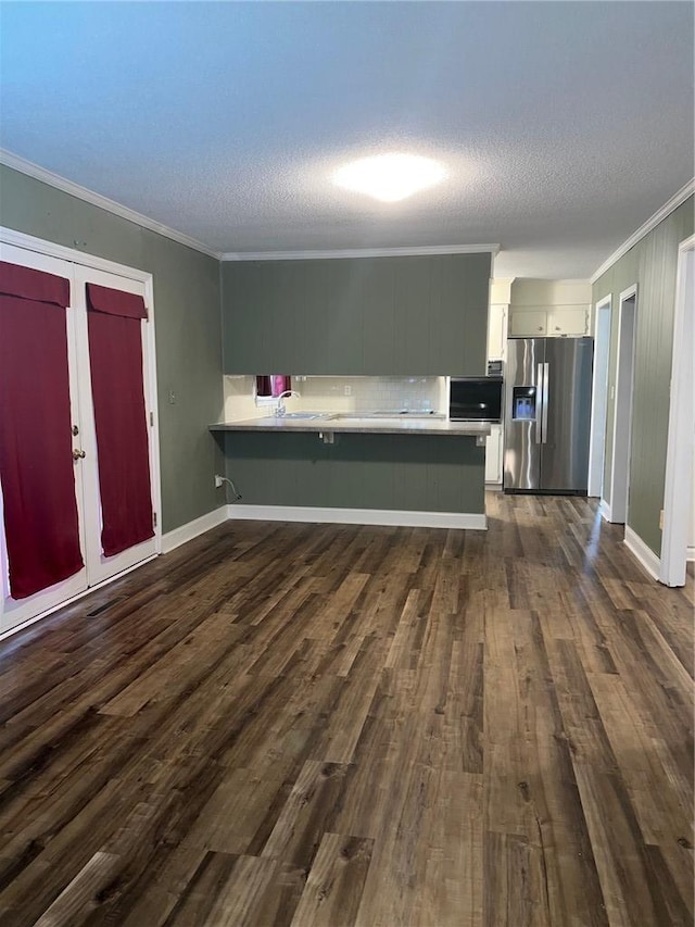 kitchen with a peninsula, dark wood-type flooring, light countertops, ornamental molding, and stainless steel fridge