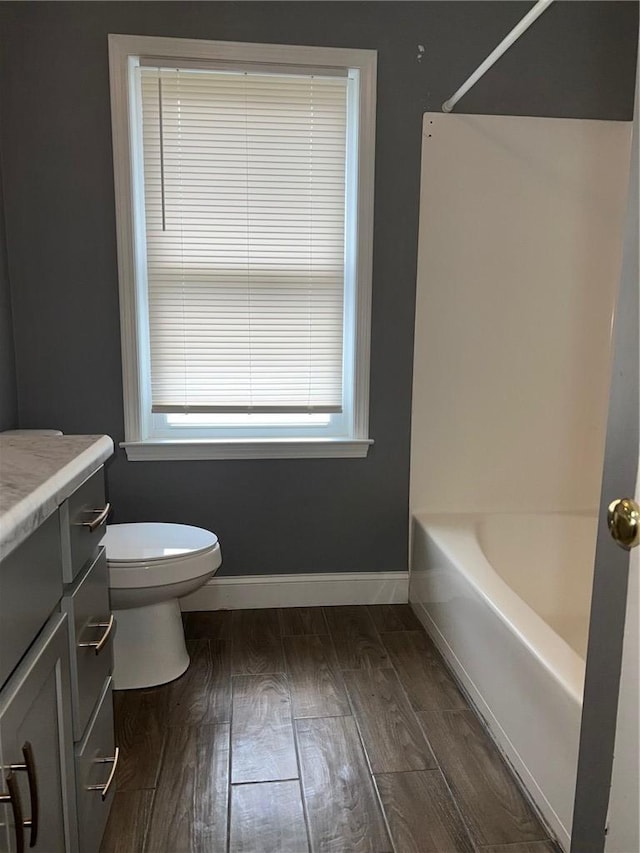 full bath with toilet, wood finished floors, vanity, baseboards, and shower / washtub combination