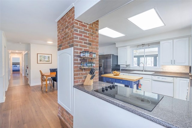 kitchen featuring stainless steel refrigerator with ice dispenser, black electric stovetop, tasteful backsplash, a sink, and white dishwasher