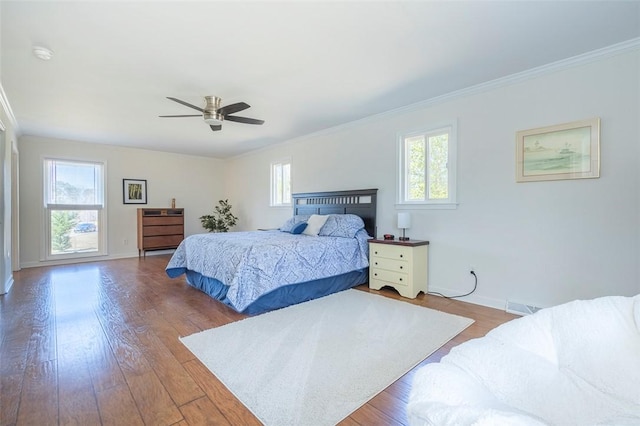 bedroom with crown molding, visible vents, baseboards, and wood finished floors