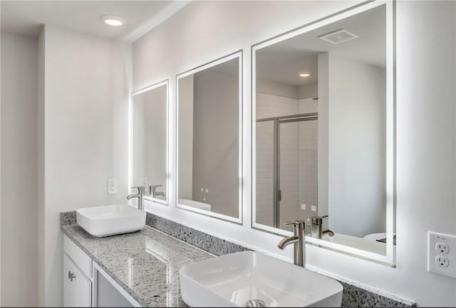 full bathroom with toilet, a sink, visible vents, and a shower stall