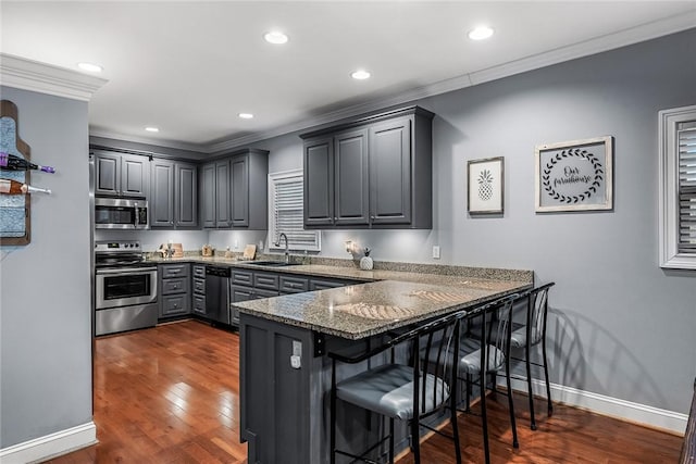 kitchen with a breakfast bar area, a peninsula, a sink, ornamental molding, and appliances with stainless steel finishes