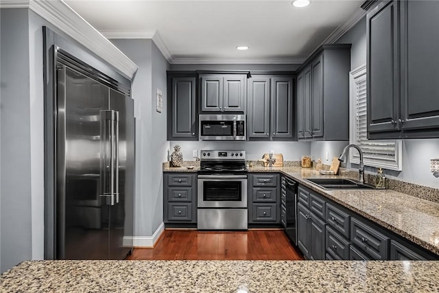 kitchen with light stone counters, stainless steel appliances, a sink, dark wood finished floors, and crown molding