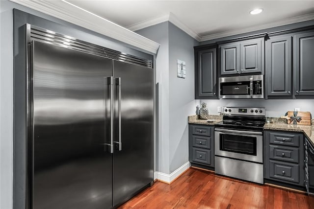 kitchen with dark wood-type flooring, baseboards, appliances with stainless steel finishes, light stone countertops, and crown molding