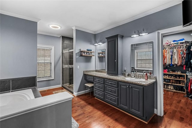 full bathroom with a walk in closet, crown molding, a shower stall, vanity, and wood finished floors