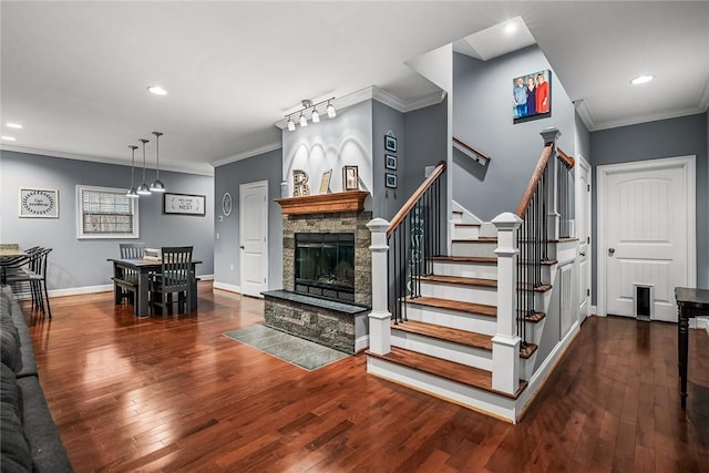 staircase featuring wood-type flooring, crown molding, a stone fireplace, and baseboards