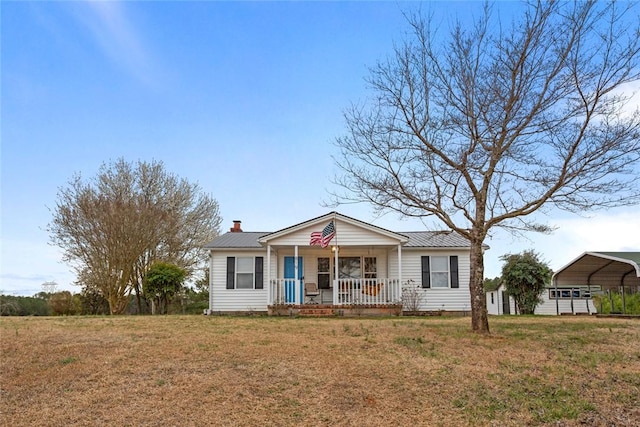 view of front of home with a porch, a detached carport, metal roof, and a front yard