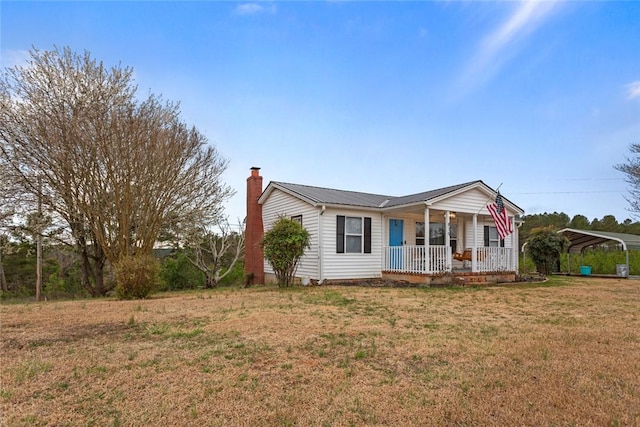 ranch-style home with metal roof, a porch, a detached carport, a chimney, and a front yard