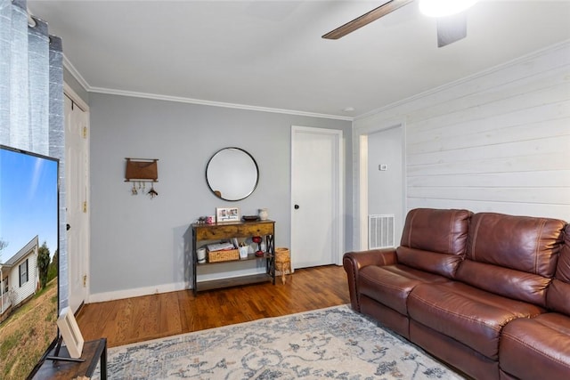 living area featuring wood finished floors, visible vents, baseboards, a ceiling fan, and ornamental molding